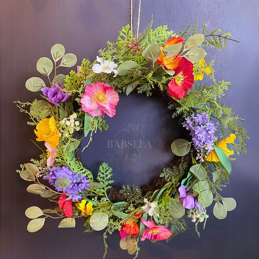 Colorful floral wreath with pink, yellow, red, purple, and white flowers, accented with lush greenery and eucalyptus leaves, hanging against a dark background