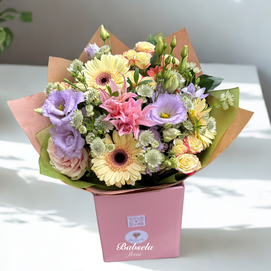 Bouquet of flowers in a pink box with 'Babsela' branding on a white surface.